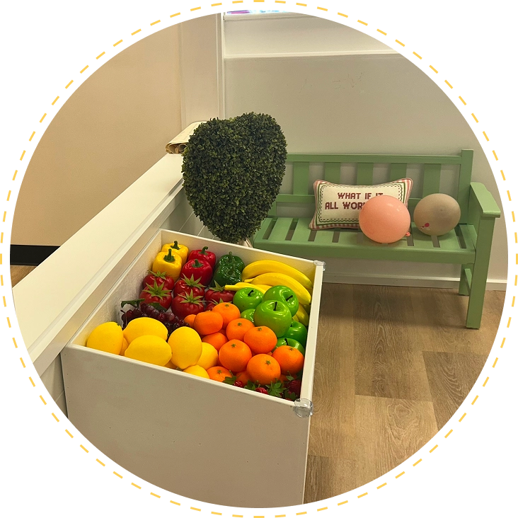 Colorful fruit display in a white box next to a green bench with a heart-shaped plant.