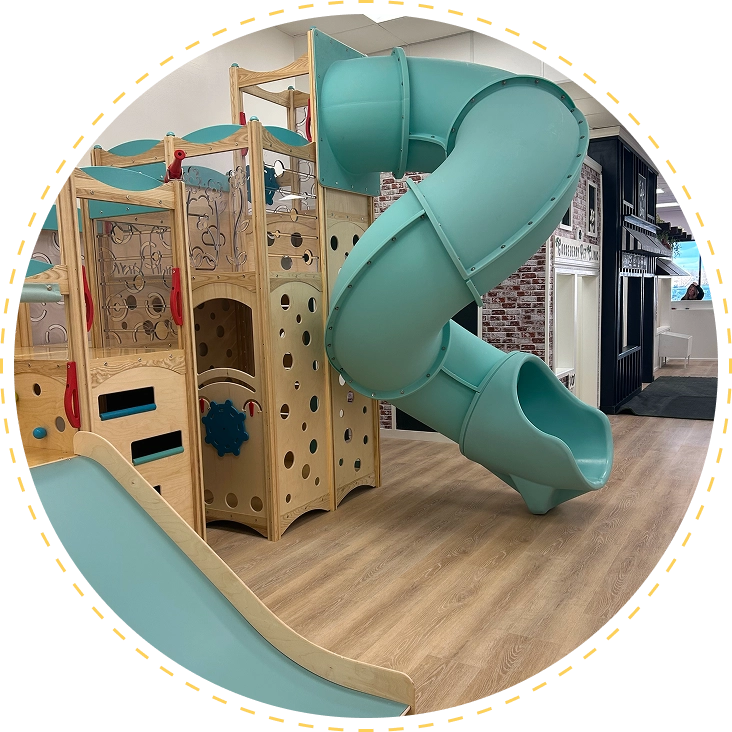 Indoor playground with wooden climbing structure and green spiral slide.